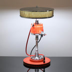 Vintage-style lamp with orange base and metal components on a reflective surface.