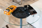 Two toy cars on a glass table with a large gear in the center.