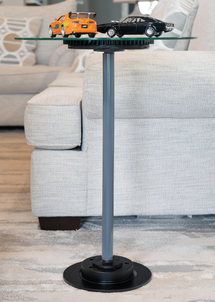 Glass side table with a black base in a living room setting, featuring two model cars on top.