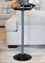 Glass side table with a black base in a living room setting, featuring two model cars on top.