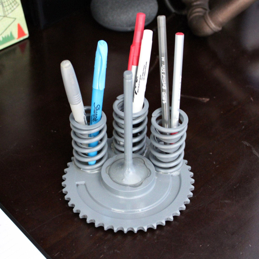 Gray gear-shaped pen holder with pens on a wooden surface