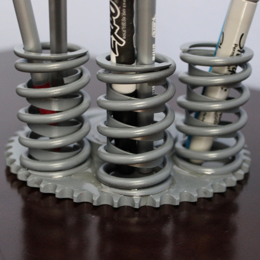 Pencil holder made from metal springs on a dark surface with a white background