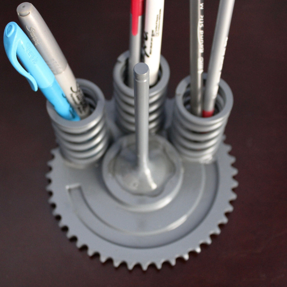Metal gear pen holder with multiple pens on a dark surface