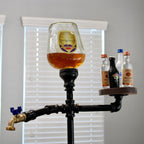 Decorative stand with a glass of beer and bottles against a window with blinds.