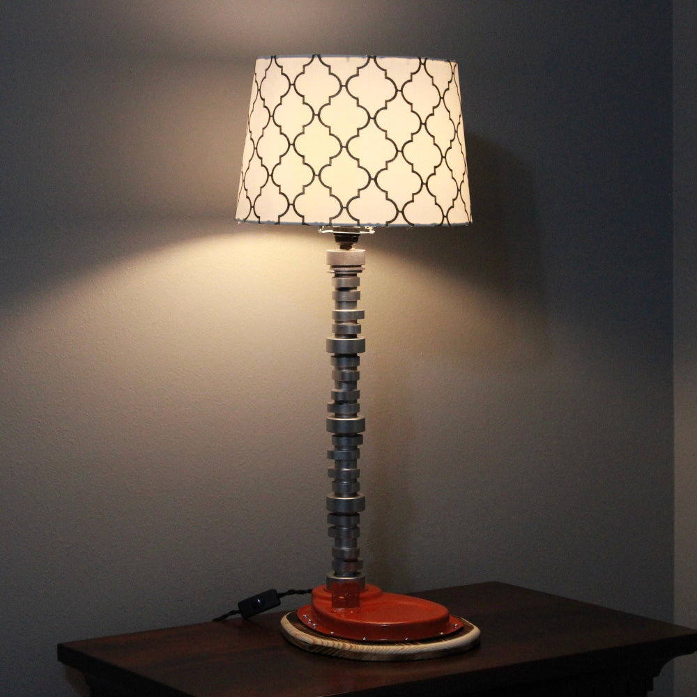 Decorative table lamp with a patterned shade on a wooden surface against a dark wall.