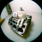 Small white robot sitting on a mechanical engine block with a business card on a light surface.