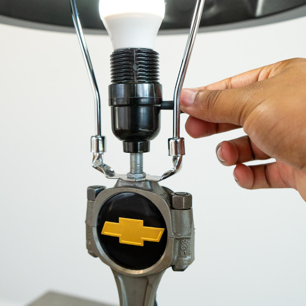 Hand adjusting a light bulb in a fixture with a Chevrolet logo on a white background