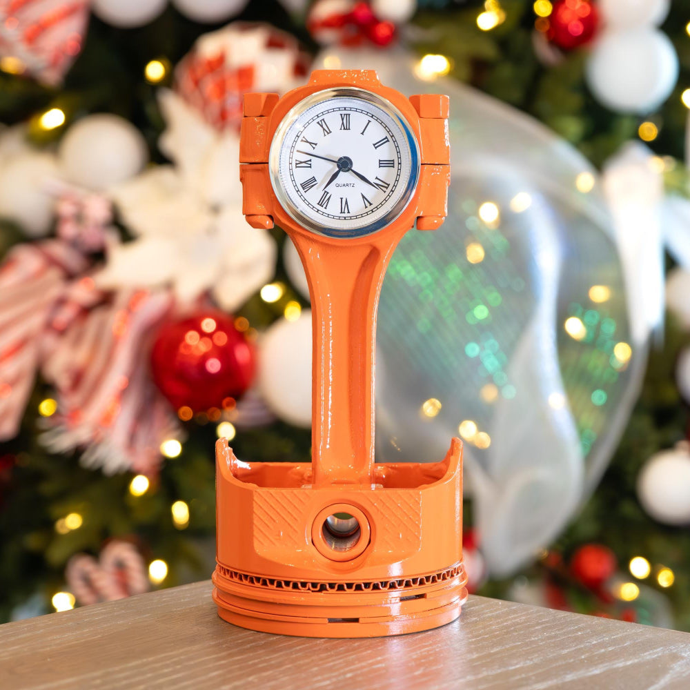 Orange clock-shaped lamp on a table with a Christmas tree in the background