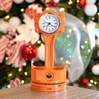 Orange clock-shaped lamp on a table with a Christmas tree in the background