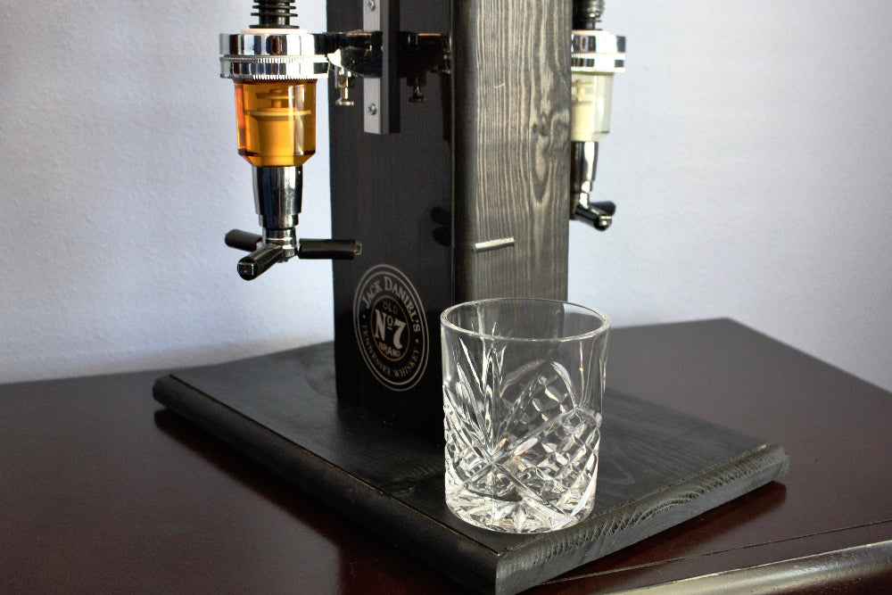 Beverage dispenser with two taps and a glass underneath on a wooden surface.