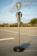 Outdoor lamp with a light bulb on a stand in an open area with trees in the background