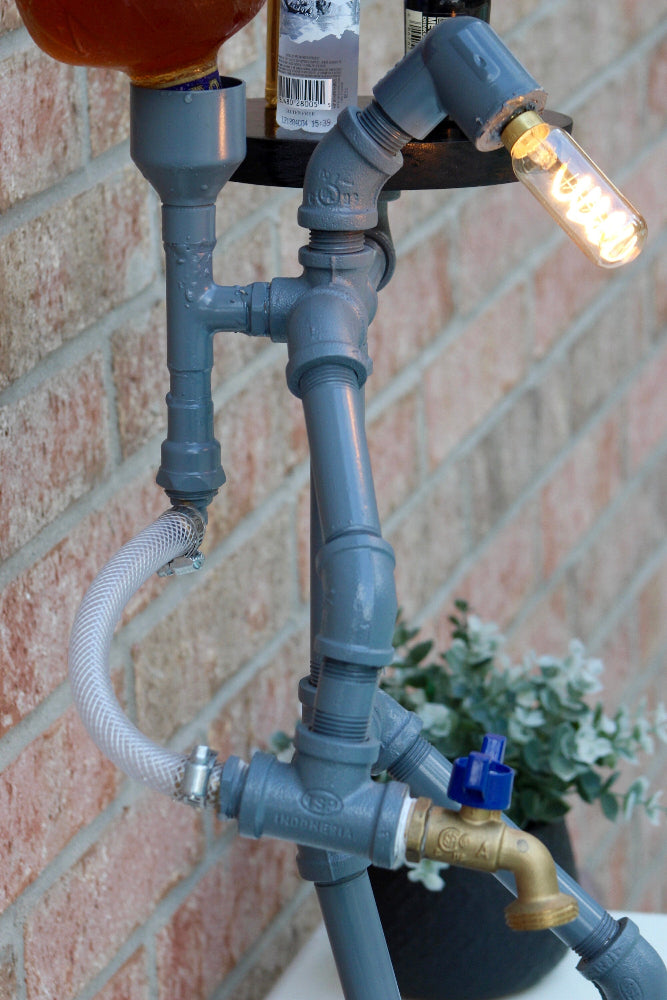 Upcycled lamp made from gray pipes and fittings against a brick wall.