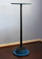 Metal stand with a round blue base against a gray wall.