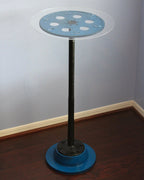 Blue and black industrial-style table with round top and pedestal base in a room.
