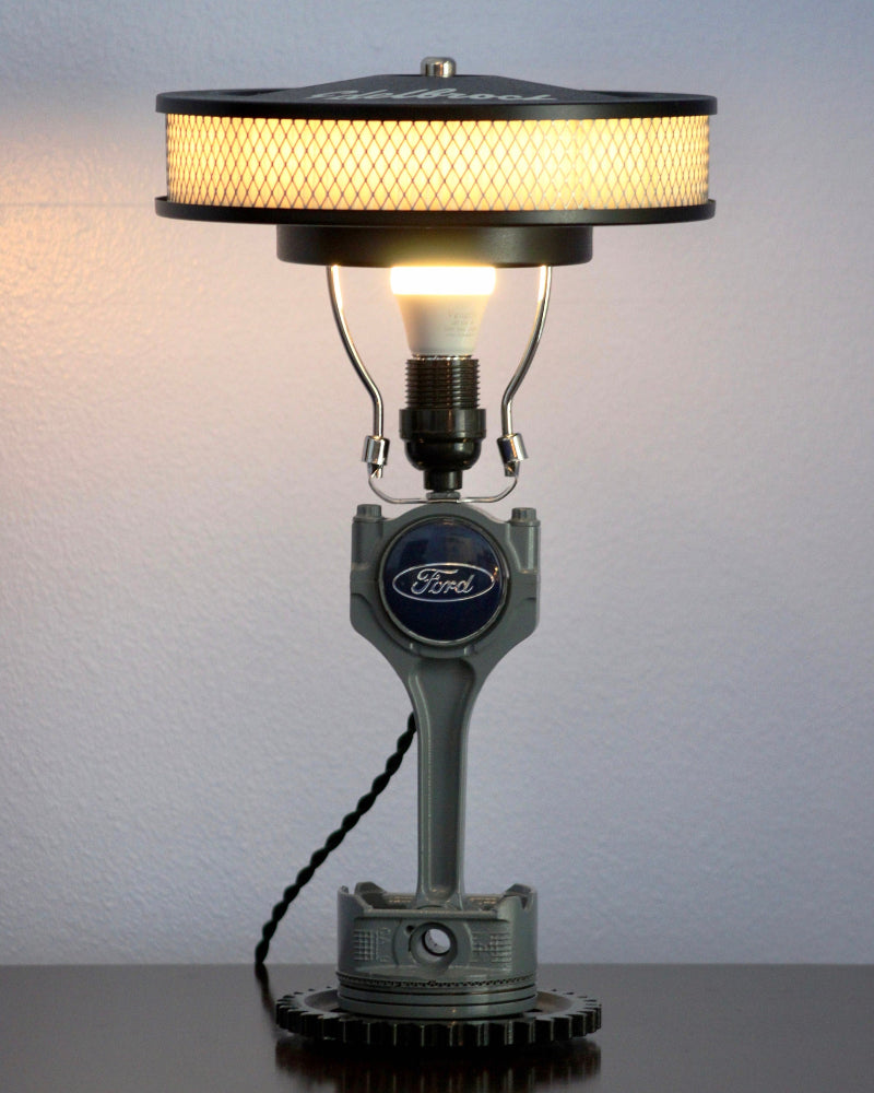 Table lamp made from a car engine part with a Ford logo, featuring a light bulb inside.