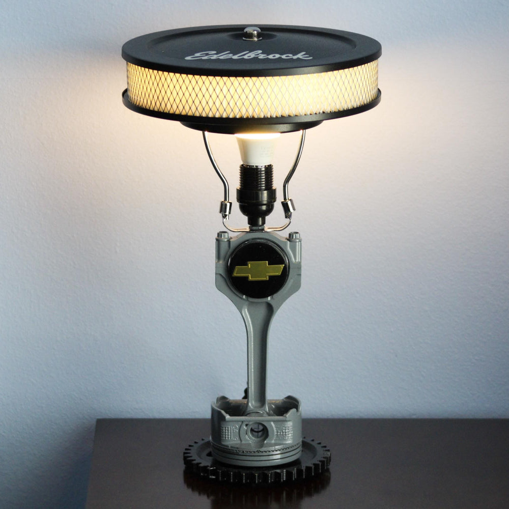 Lamp made from automotive parts on a dark surface with a light gray background