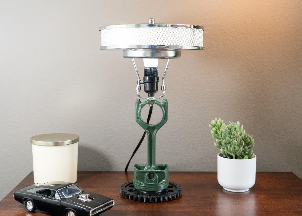 Table lamp with vintage design on a wooden surface, next to a small model car and a potted plant.