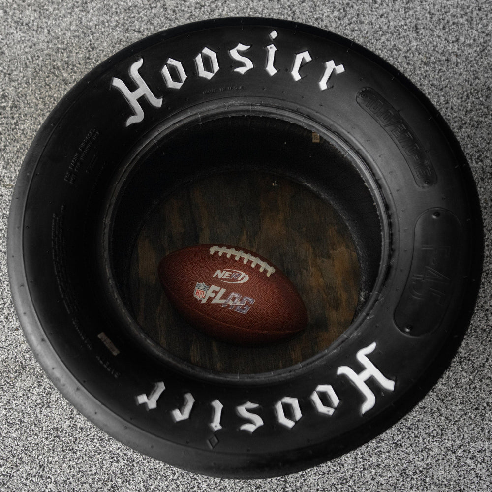 Black tire with 'Hoosier' branding and a football inside on a textured gray background