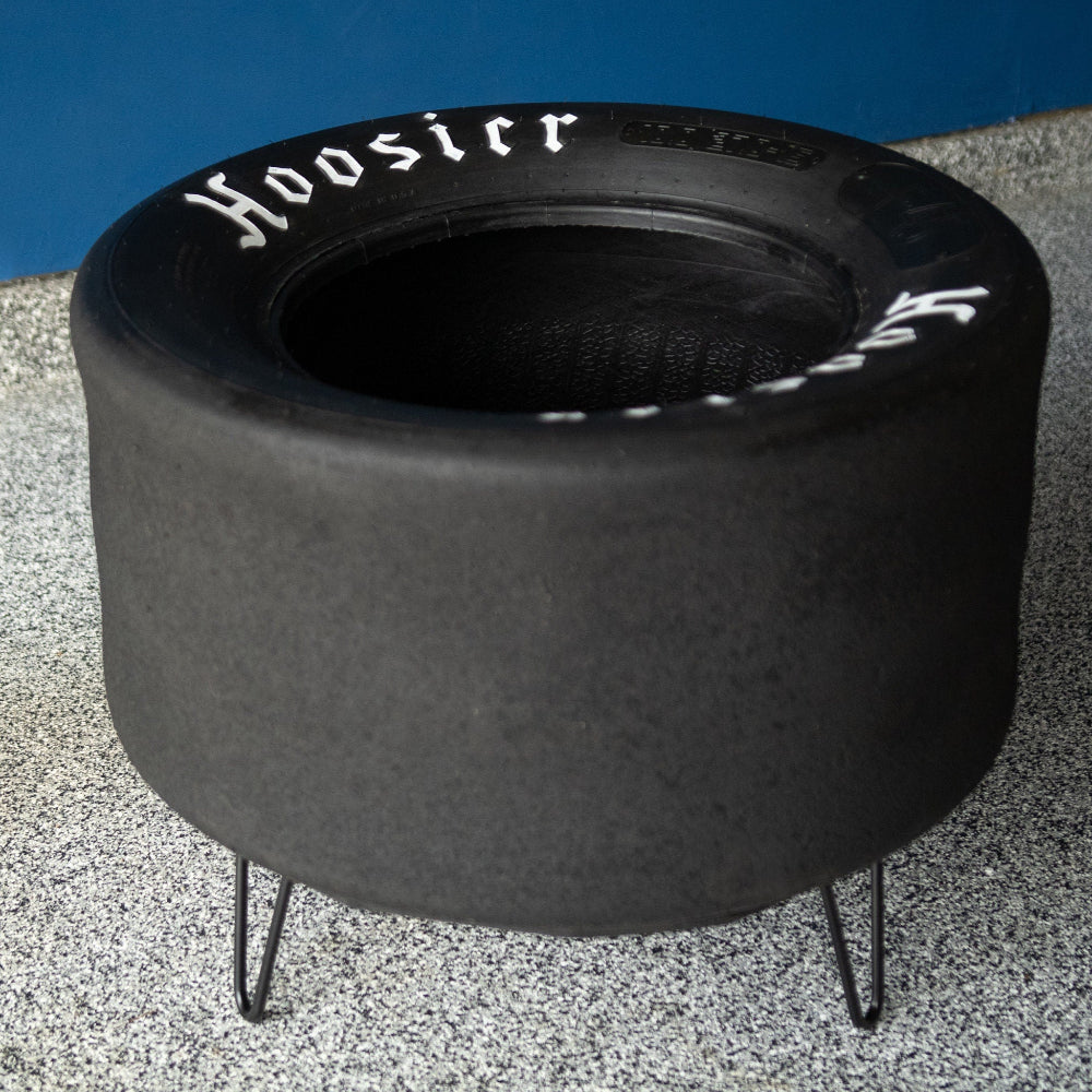 Black tire-shaped fire pit with 'Hoosier' branding on a concrete surface.