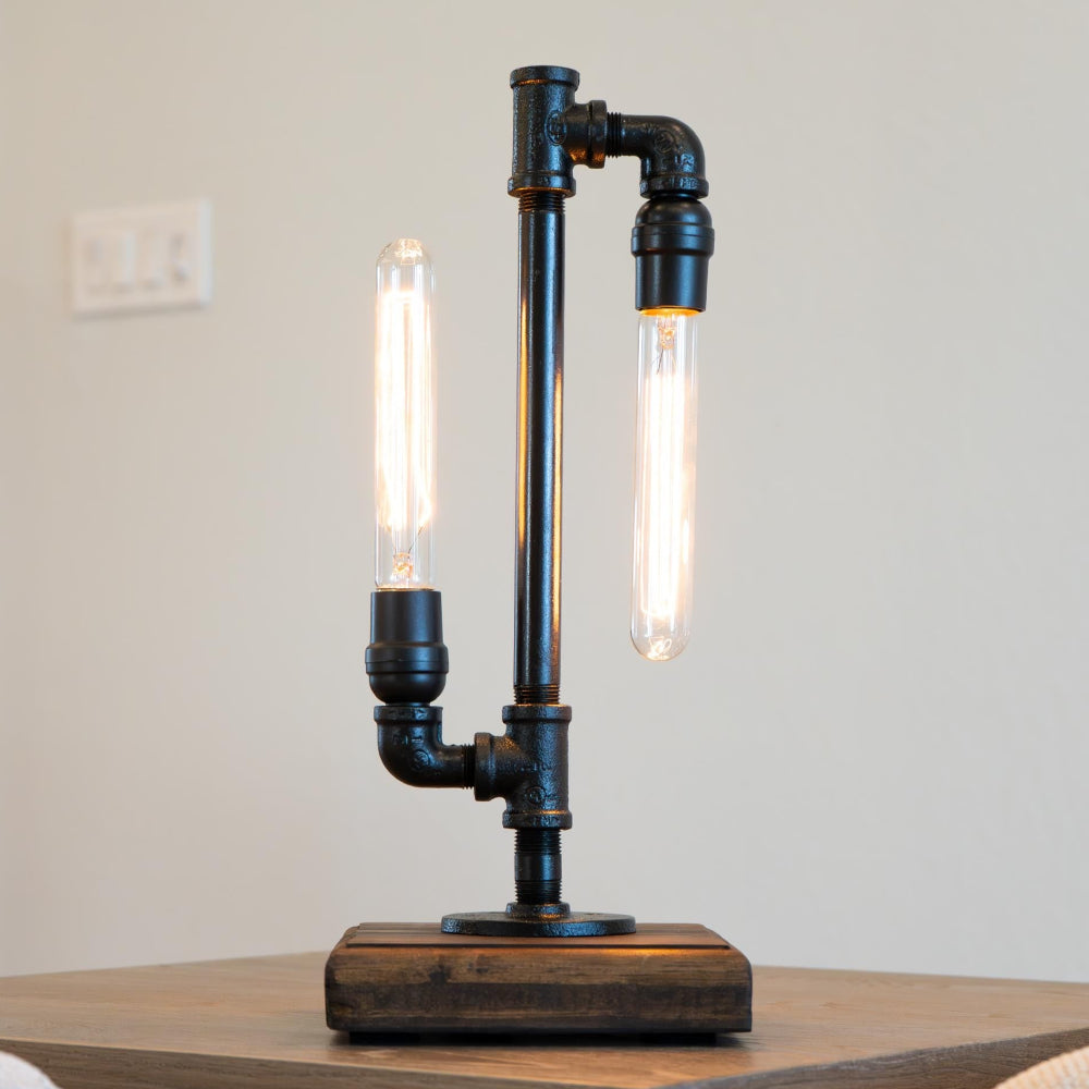 Industrial-style table lamp with black metal pipes on a wooden surface.