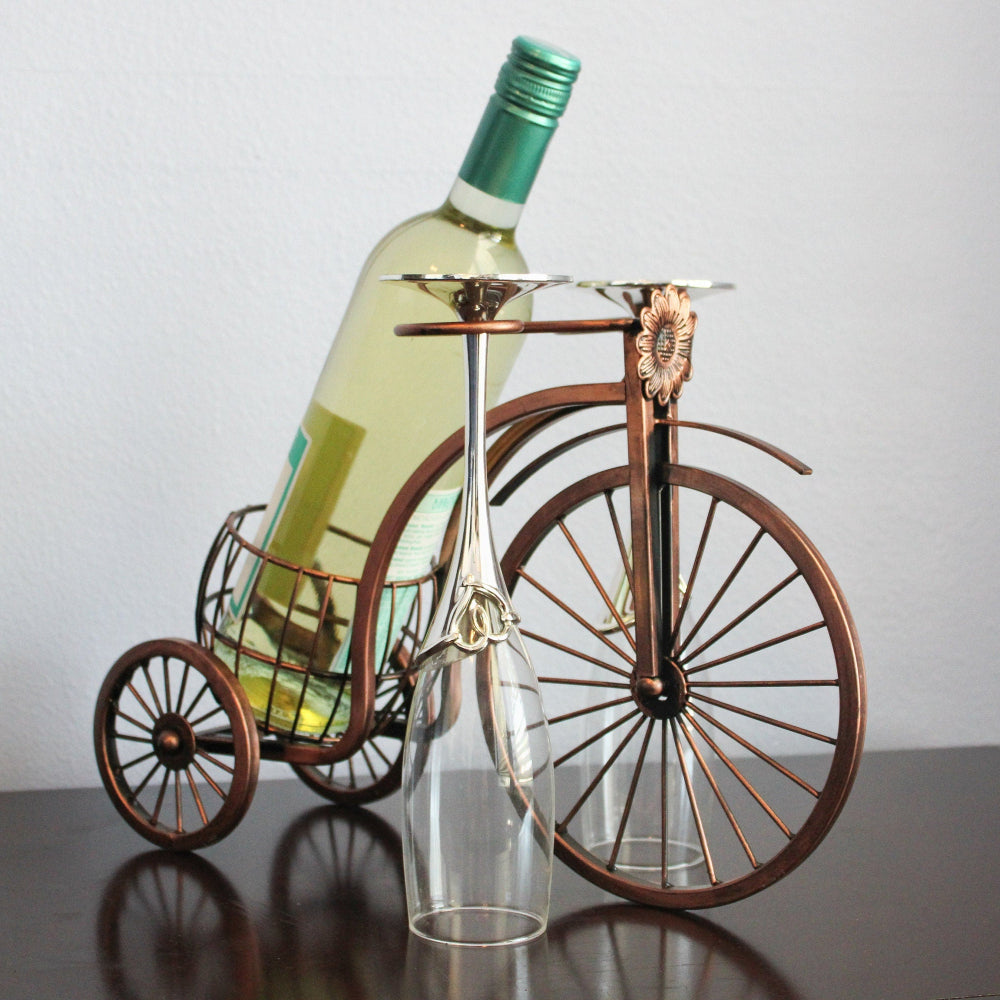 Wine bottle holder shaped like a vintage bicycle with a wine bottle and glass on a plain background