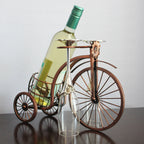 Wine bottle holder shaped like a vintage bicycle with a wine bottle and glass on a plain background