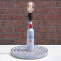 Lamp made from a Michelob Ultra beer bottle on a textured base against a brick wall.