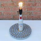 Bottle lamp made from a vodka bottle with a light bulb on a white surface and brick wall background.