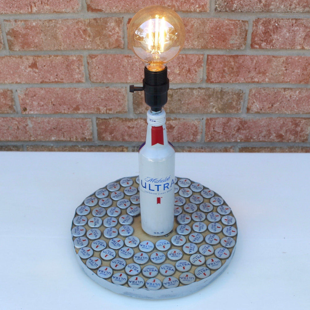 Bottle lamp made from a vodka bottle with a light bulb on a white surface and brick wall background.