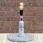 Alcohol bottle repurposed as a lamp with a light bulb against a brick wall.