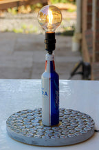 Lamp made from a beer bottle with a light bulb, placed on a concrete base.
