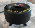 Coffee table made from a race car tire with 'Good Year' branding and a toy car on top.