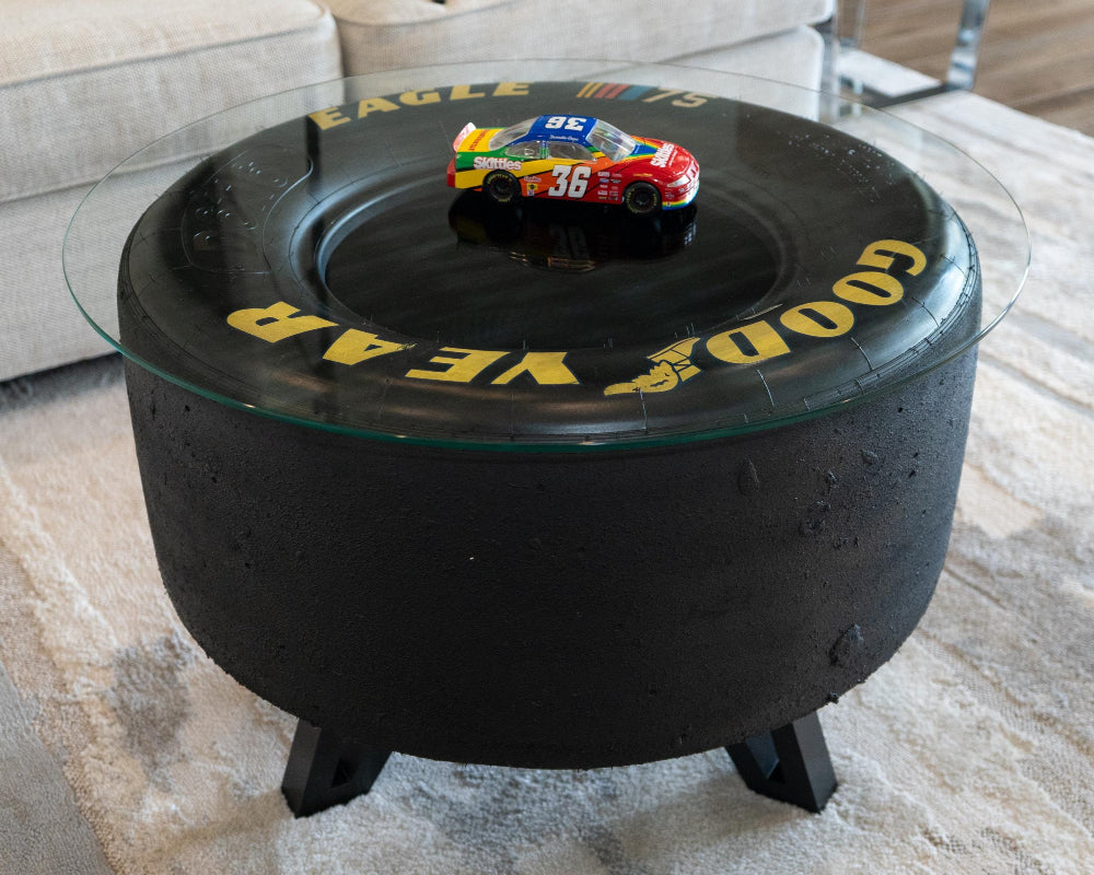 Coffee table made from a race car tire with 'Good Year' branding and a toy car on top.