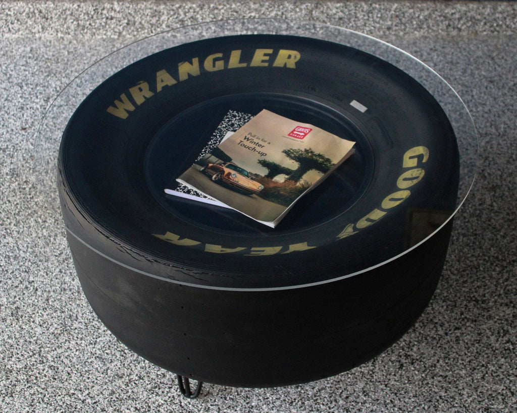Round black tire-shaped ottoman with 'Wrangler' branding on a gray floor.