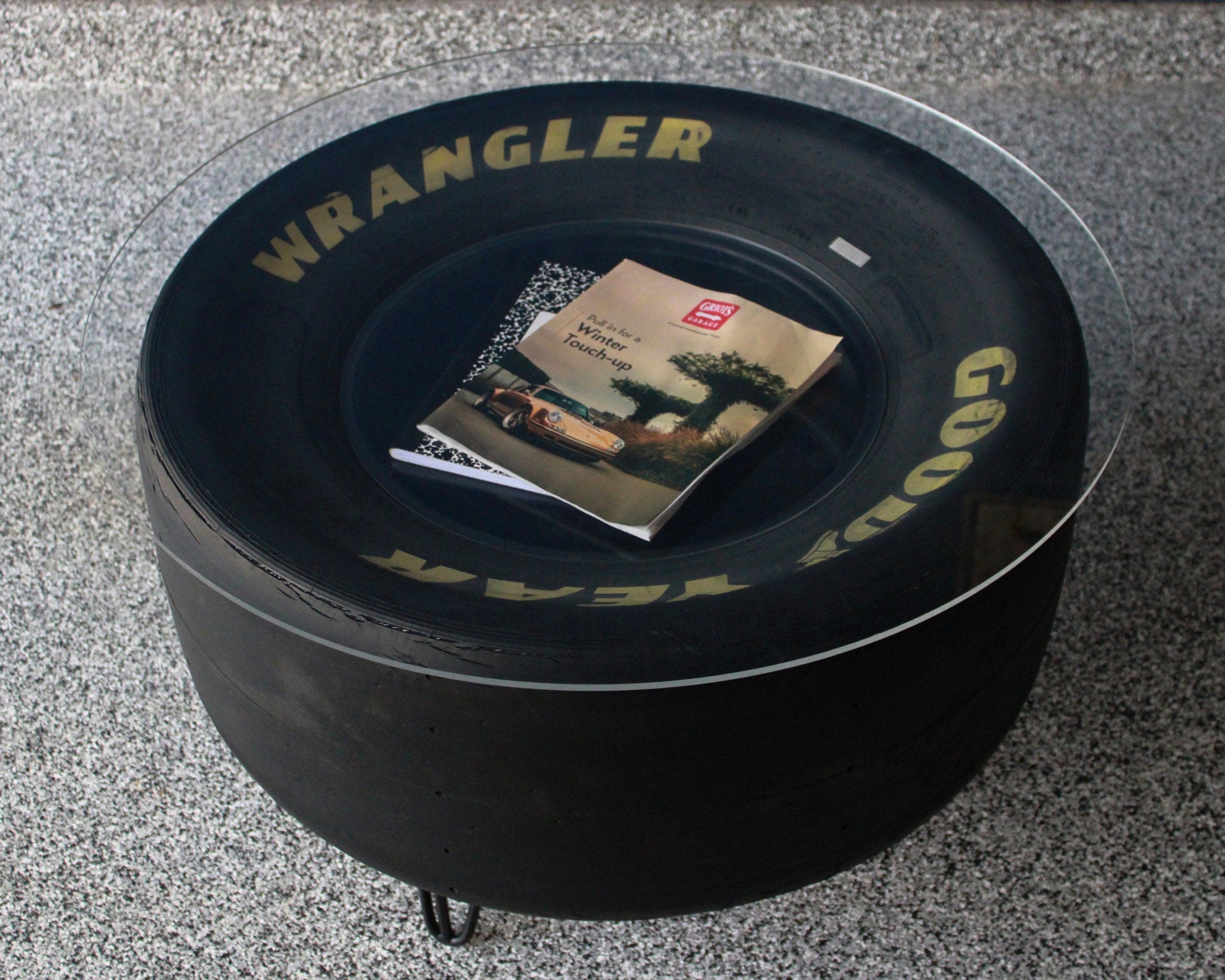 Round black tire-shaped ottoman with 'Wrangler' branding on a gray floor.