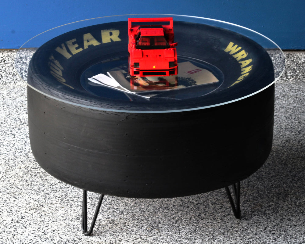 Black tire-shaped table with a red toy truck on top, against a blue wall.