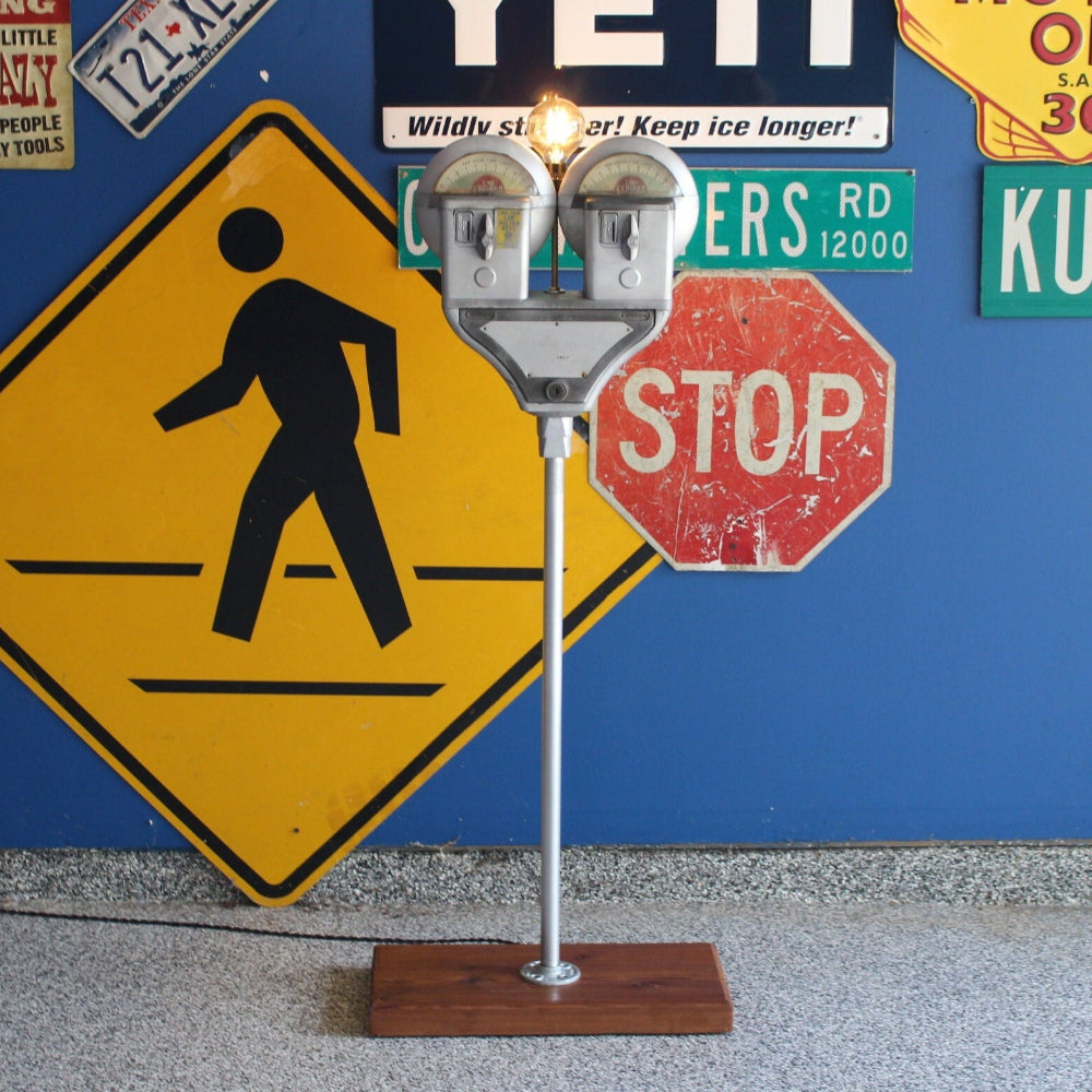 Parking meter lamp with two coin slots next to wall with street signs 