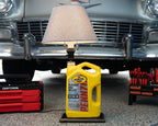 Yellow Pennzoil bottle with a lamp on a car bumper, surrounded by tools and equipment.