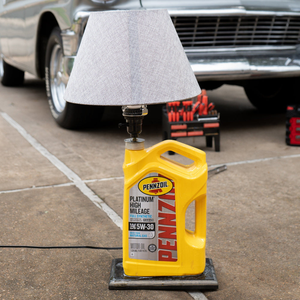 Yellow Pennzoil oil bottle on a stand with a car and tools in the background