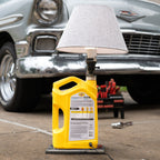 Yellow oil jug on a car lift with a classic car in the background