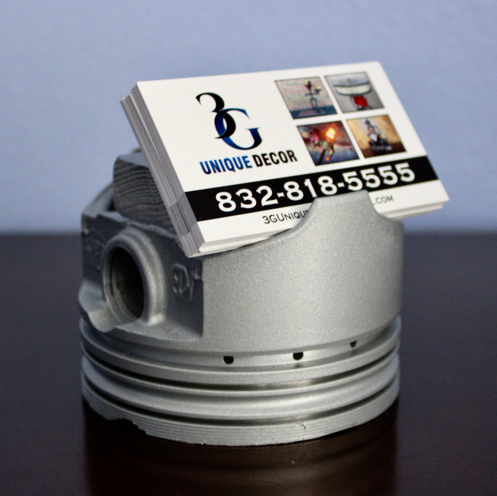 Business card holder shaped like a piston with a business card on a dark surface