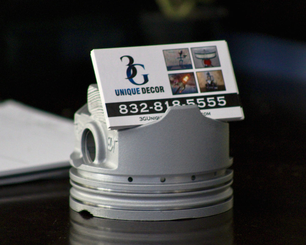 Business card holder shaped like a piston with a business card on a dark surface