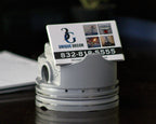Business card holder shaped like a piston with a business card on a dark surface