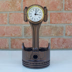Piston-shaped clock on a white surface with a brick wall background