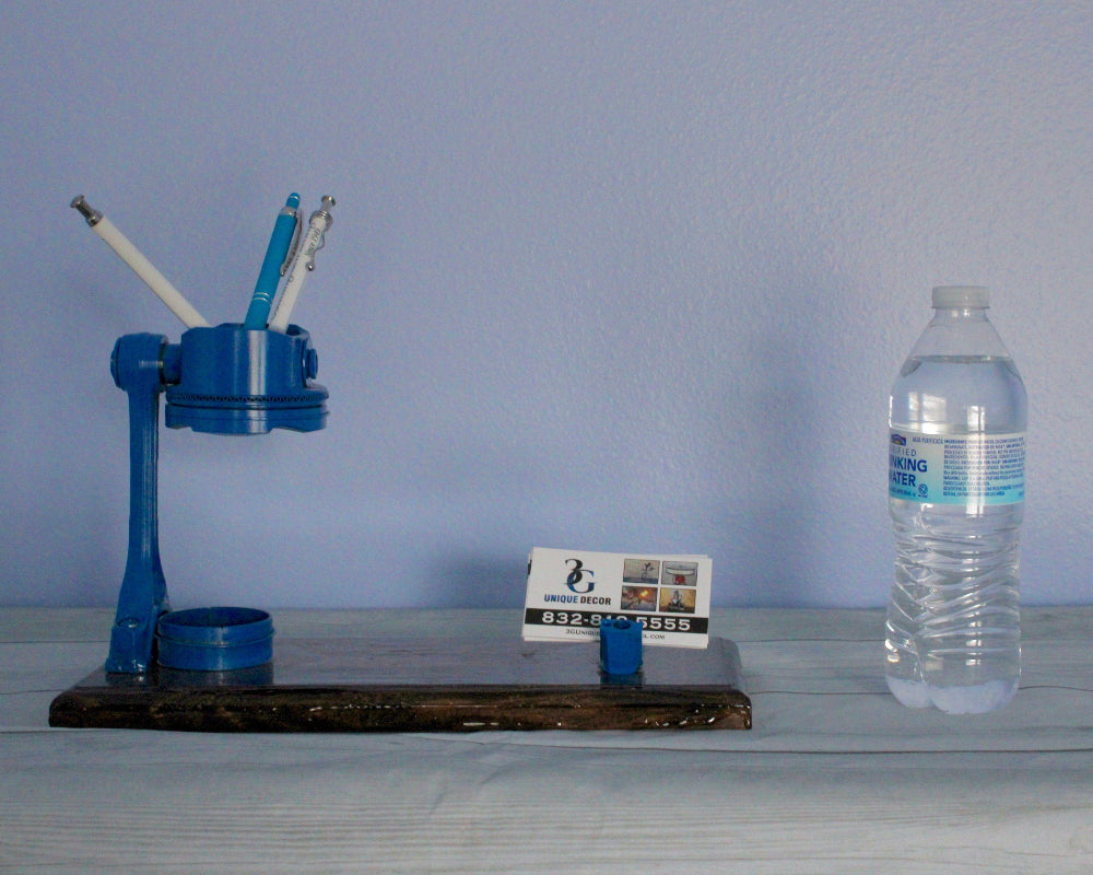 Blue mechanical desk organizer with pens and a bottle of water on a wooden surface against a blue wall.