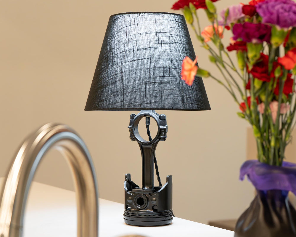 Black lamp with a unique design on a table next to a vase of flowers.