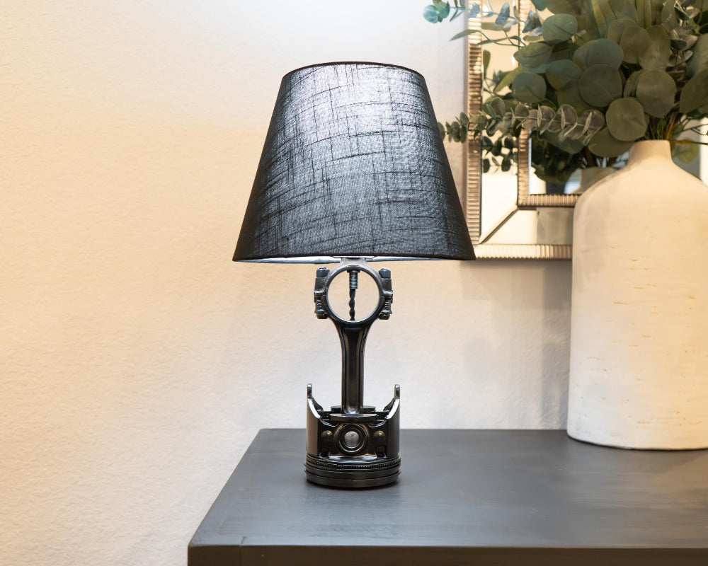 Table lamp with black shade on a surface next to a vase with greenery