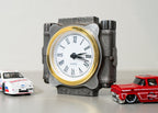 Decorative clock with Roman numerals and two toy cars on a light background