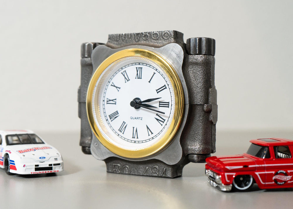 Decorative clock with Roman numerals and two toy cars on a light background