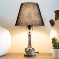 Table lamp with a dark shade on a wooden surface with decorative items.